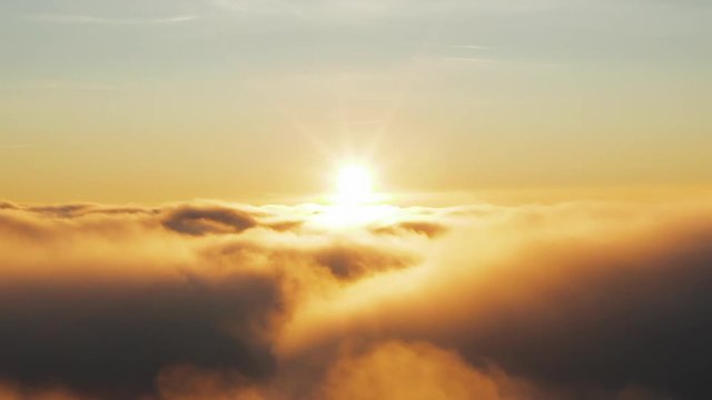 Aerial view flying through clouds with sunset center frame illuminating the cloud tops.