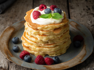 Pancake with vanilla cream, blueberries and raspberries. Side view, macro, close-up. Dark moody old rustic wooden background.