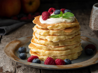Pancake with vanilla cream, blueberries and raspberries. Side view, macro, close-up. Dark moody old rustic wooden background.