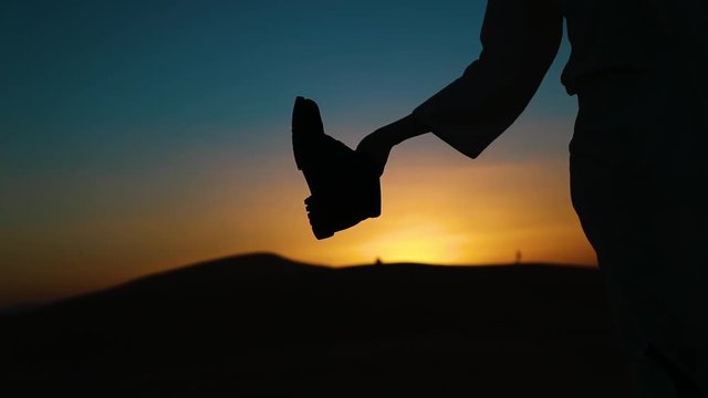 Slowmotion shot, emptying a boot, filled with sand during golden hour.