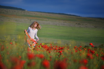 Blonde with long hair in white dress on background of red poppy field