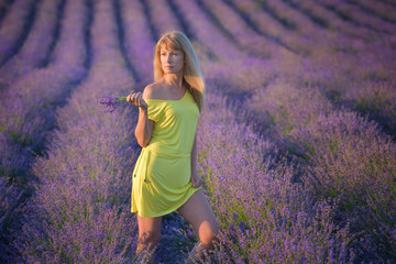 Young beautiful woman with long blond hair on lavender field. Blonde with long hair in yellow dress on background of lilac field at sunset