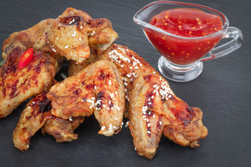Baked chicken wings with sesame seeds and sweet chili sauce on dark background