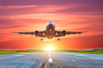 Fototapeta na wymiar Airplane landing on the runway behind a bright sunset with a pink sky