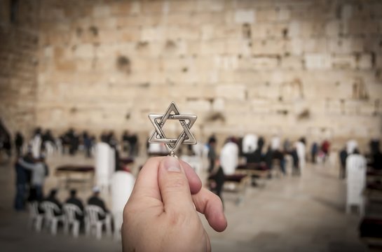 JERUSALEM, ISRAEL. February 15, 2019. Hand holding a Star of David, a Jewish national and religious symbol in front of the Western wall of the Jewish Temple in the Old city of Jerusalem.
