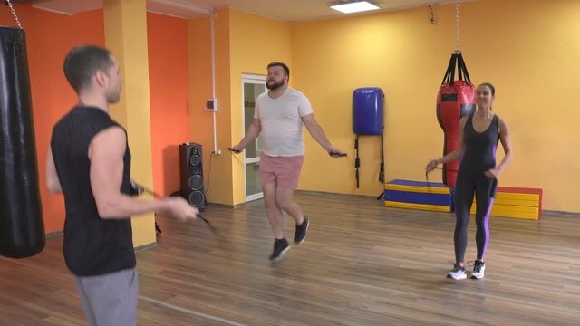 Bearded man and girl jump on a rope in the gym under the supervision of a trainer, warm up before training boxing, jumping-rope