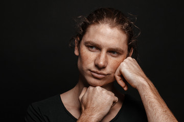 Portrait of a handsome long-haired man with drawn hair and freckles wearing a black T-shirt