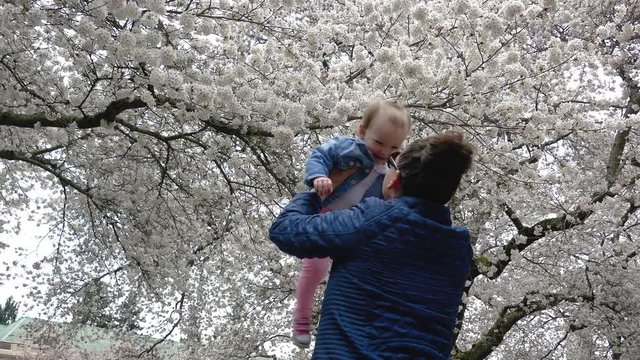 Mother Tossing Baby in Air Below Cherry Blossom Tree