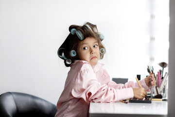 Cute little girl playing with her mother's cosmetic in front of the mirror at home