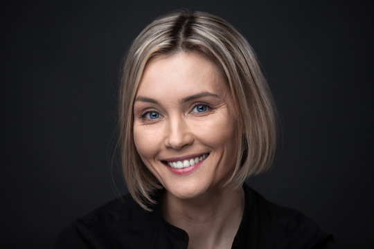 Beautiful Middle-aged Woman On A Gray Background In A Black Blouse.