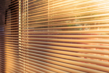 morning sunlight at sunrise shining through the slats of horizontal venetian blinds.