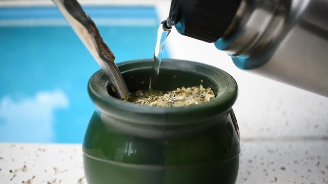 Pouring water for a typical argentinian mate tea near a pool in the summer.