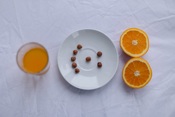 orange cut in half on a white plate on a white background with a smile of nuts and a glass of juice