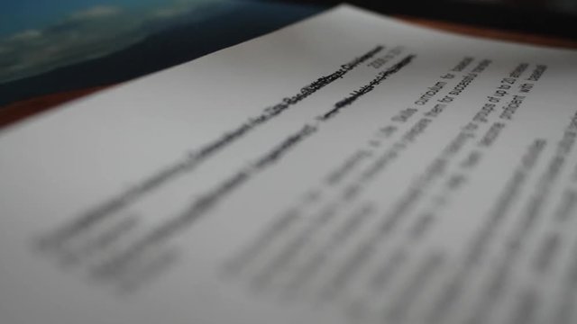A male hand edits a printed document with a pen on a wooden table.
