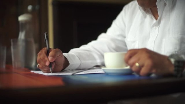 A male hand edits a printed document with a pen on a wooden table.