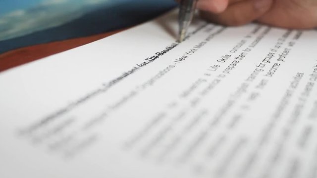 A male hand edits a printed document with a pen on a wooden table.