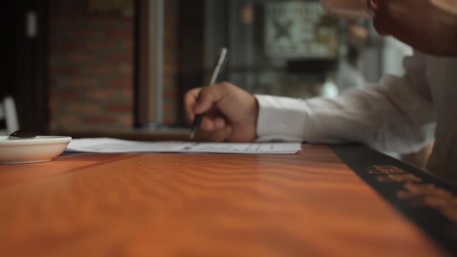 A male hand edits a printed document with a pen on a wooden table.