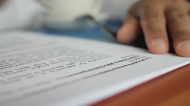 A male hand edits a printed document with a pen on a wooden table.