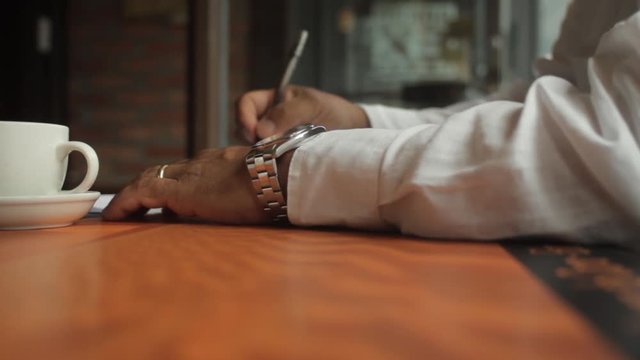 A male hand edits a printed document with a pen on a wooden table.