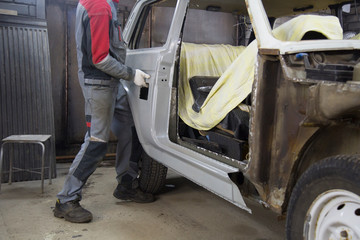 Auto repairman plastering autobody bonnet. Auto mechanic worker painting car in a paint chamber during repair work. 