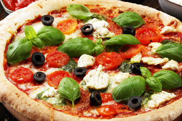 Pizza with tomatoes, mozzarella cheese, black olives and basil. Delicious italian pizza on wooden pizza board.