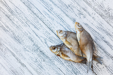 Three dried fish bream lie on a light wooden table.