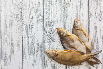 Three dried fish bream lie on a light wooden table.
