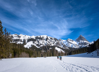 Fototapeta na wymiar Adults snowshoeing on snowy plateau Kaiserau with mountain Admonter Kalbling