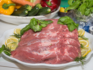 Piece of Raw Beef on a Plate Garnished with Slices of Lemon and Basil and Rosemary