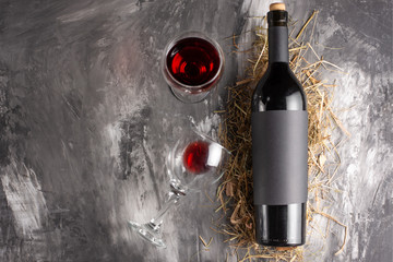 A bottle of red expensive wine with a black blank label on a dark texture. And a glass of red wine. A mock up bottle of wine. View from above. Flat lay. with space for text