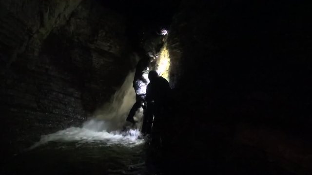 Cavers work themselves and their gear down an underground waterfall
