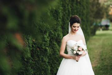 Beautiful bride in elegant white dress holding bouquet posing in park