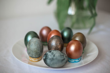 Beautiful colored shiny easter eggs on the white plate. Pink tulips flowers bouquet. Happy easter concept.