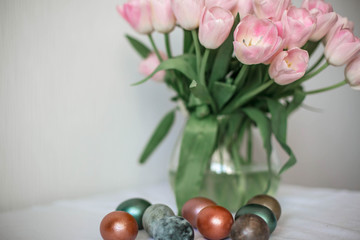 Beautiful colored shiny easter eggs on the white plate. Pink tulips flowers bouquet. Happy easter concept.