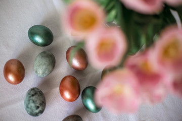 Beautiful colored shiny easter eggs on the white plate. Pink tulips flowers bouquet. Happy easter concept.