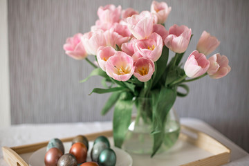 Beautiful colored shiny easter eggs on the white plate. Pink tulips flowers bouquet. Happy easter concept.