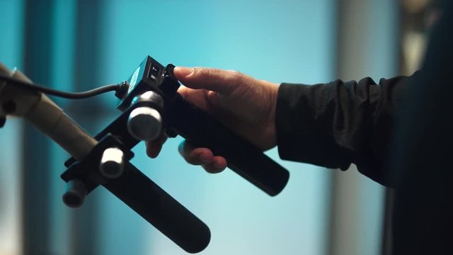 A colorful shallow depth of field moving shot of a TV Studio camera tripod zoom and focus control handle being operated by a male hand.
