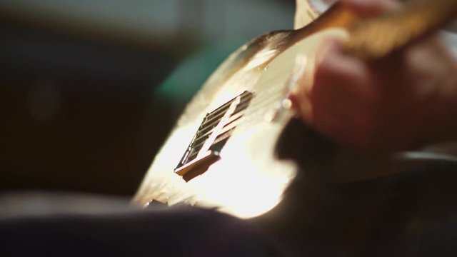 A colorful shallow depth of field close up of a Fender Telecaster with beautiful lighting reflecting off it as it is held by a sitting male in jeans and t-shirt.