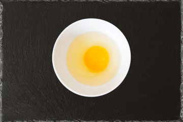  broken egg with egg shells in a bowl with black slate background
