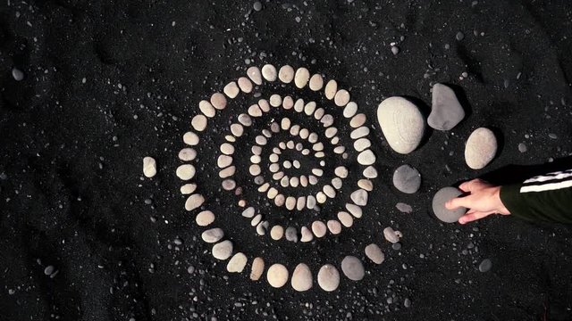 Snail pattern on black sand, made out of a stone in Iceland. Travelling and backpacking concept.
