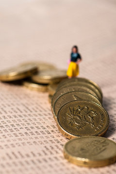 Little Figure Of A Woman Climbing Over Tumbled One Pound Coins Laid Over Share Figures