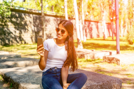 A smiling young woman sitting and using her smartphone
