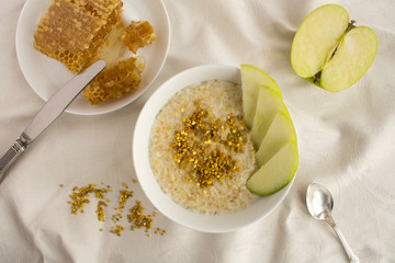 Breakfast: oatmeal with bee pollen,honey and apple in the white bowl on the textile background.Top view.