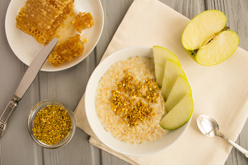 Breakfast: oatmeal with bee pollen,honey and apple in the white bowl on the grey wooden background.Top view.