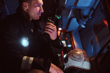 The fire brigade arrived at the night-time. Fireman in a protective uniform sitting in the fire truck and talking on the radio