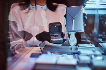 Woman assistant shows the exclusive gold necklace and ring in the luxury jewelry store