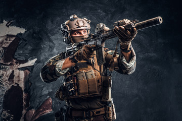 Fototapeta na wymiar Elite unit, special forces soldier in camouflage uniform holding an assault rifle with a laser sight and aims at the target. Studio photo against a dark textured wall