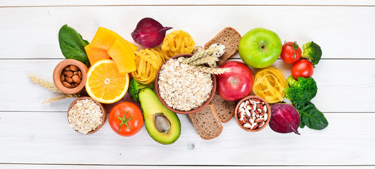 Healthy food containing carbohydrates: bread, pasta, avocados, flour, pumpkin, broccoli, beans, spinach. On a white background. Top view. Free copy space.
