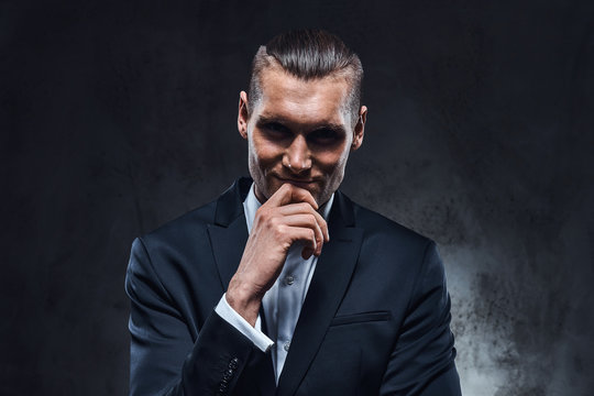 A confident businessman in black suit wearing elegant black suit. Studio shot on a dark textured wall