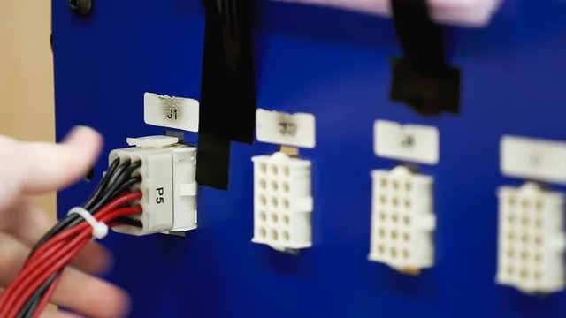 A worker operating a wire testing machine at a stock-wire factory: hands plugging the terminal part into the connector. Close-up shot.